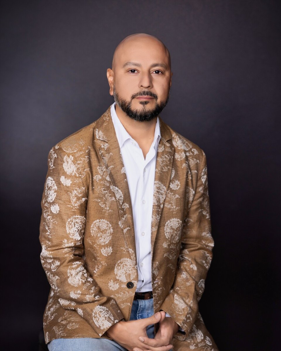 Edmund Lara, founder of Inspire Acquire, in a tan patterned jacket against a dark backdrop